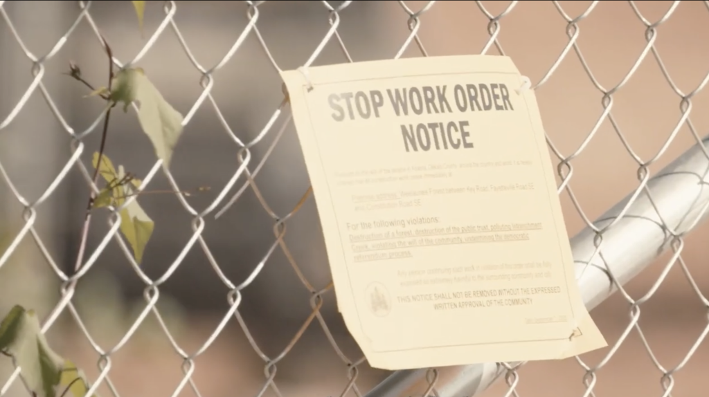 A sheet of paper with the heading "STOP WORK ORDER NOTICE" is appended to a metal fence on the Cop City construction site.